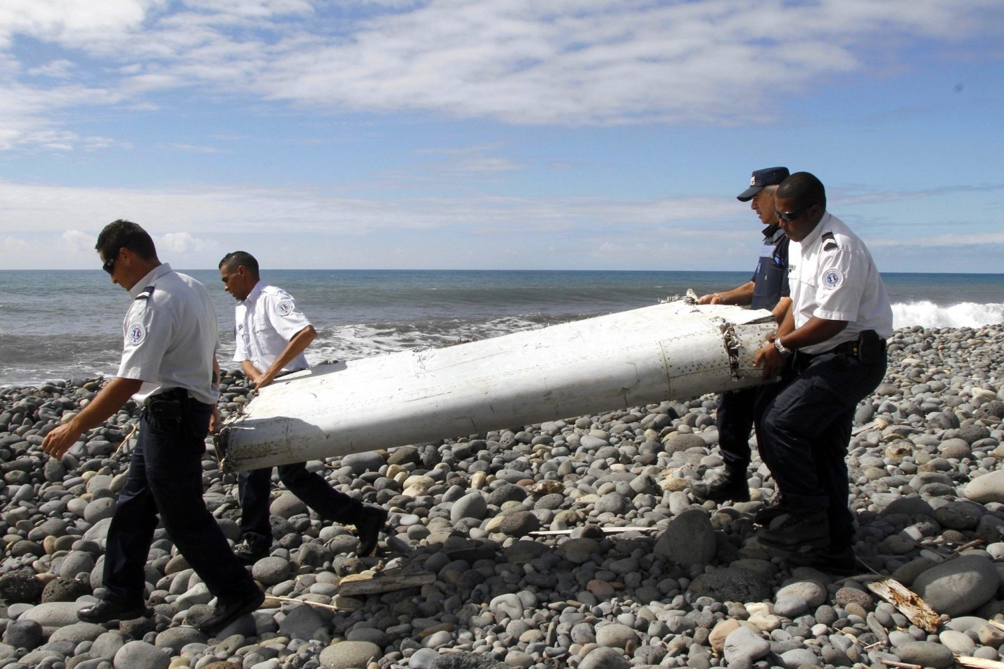 Techniker tragen ein Wrackteil, die Flügelklappe eines Flugzeugs, über einen Strand bei Saint-André, Réunion.